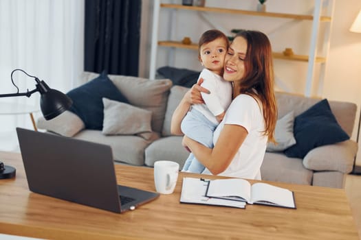 Laptop is on the table. Mother with her little daughter is at home together.