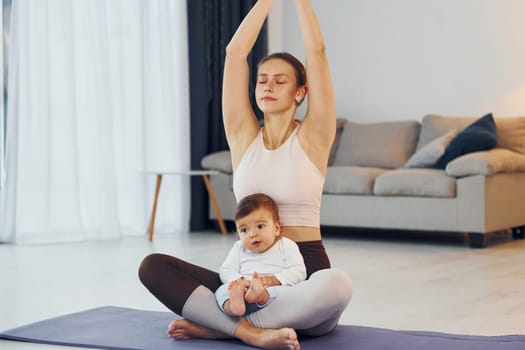 Doing yoga exercises. Mother with her little daughter is at home together.