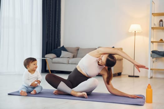 Doing yoga exercises. Mother with her little daughter is at home together.