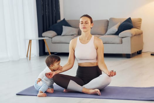 Doing exercises on the mat. Mother with her little daughter is at home together.