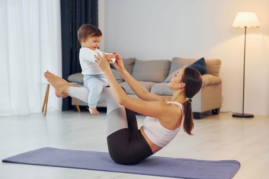 Woman laying down on mat and holding little girl. Mother with her little daughter is at home together.