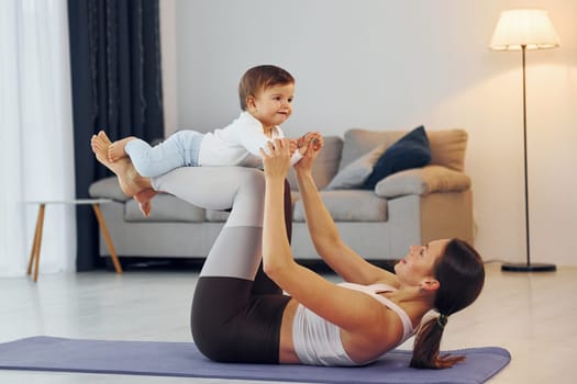 Woman laying down on mat and holding little girl. Mother with her little daughter is at home together.