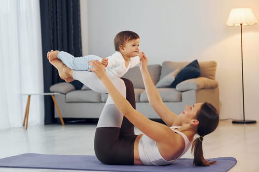 Woman laying down on mat and holding little girl. Mother with her little daughter is at home together.