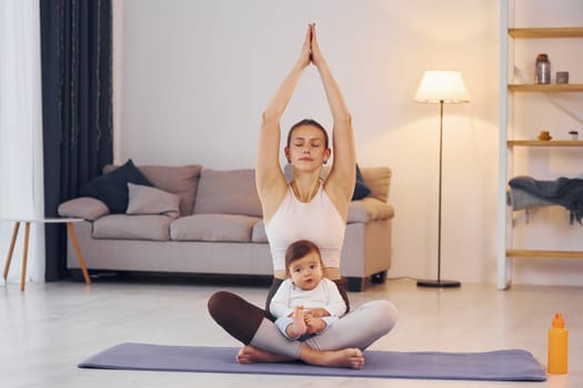 On the yoga mat. Mother with her little daughter is at home together.