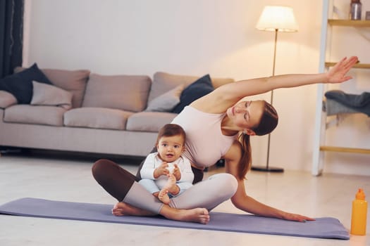 On the yoga mat. Mother with her little daughter is at home together.