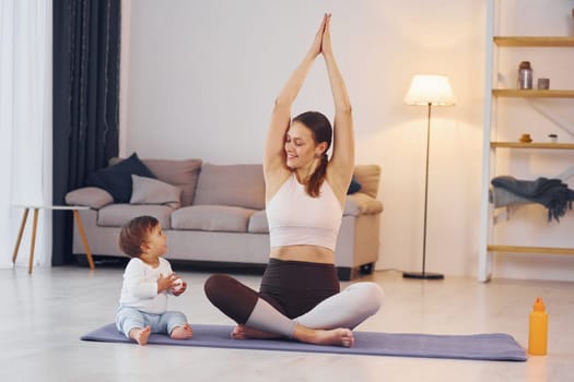 Practicing yoga. Mother with her little daughter is at home together.