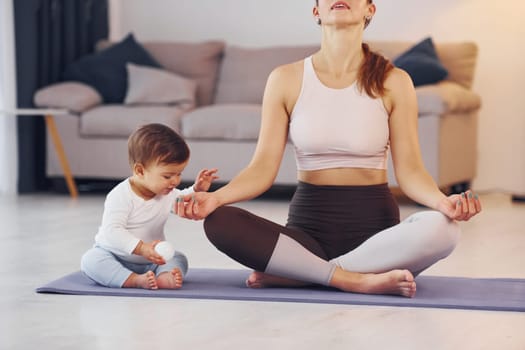 Focused at yoga exercises. Mother with her little daughter is at home together.