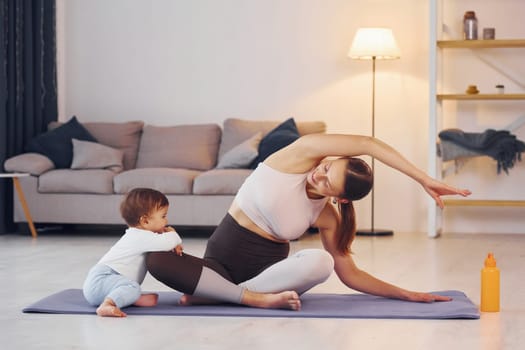 Focused at yoga exercises. Mother with her little daughter is at home together.