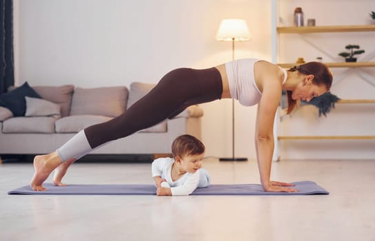 Focused at yoga exercises. Mother with her little daughter is at home together.