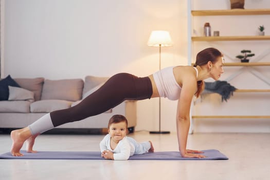 Focused at yoga exercises. Mother with her little daughter is at home together.