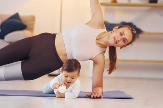 Woman doing exercises. Mother with her little daughter is at home together.