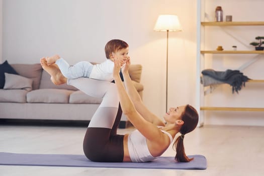 Side view of woman that doing exercises with little girl. Mother with her little daughter is at home together.