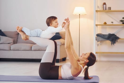 Side view of woman that doing exercises with little girl. Mother with her little daughter is at home together.