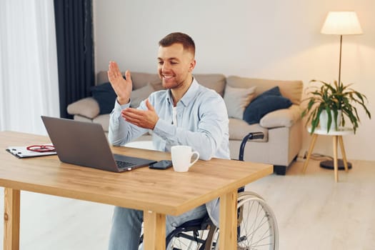 Laptop on the table. Disabled man in wheelchair is at home.