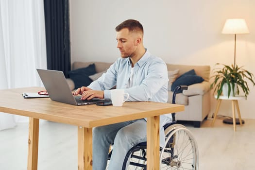 Laptop on the table. Disabled man in wheelchair is at home.