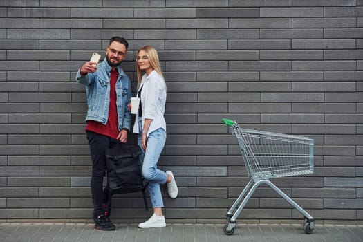 With shopping cart. Young stylish man with woman in casual clothes outdoors together. Conception of friendship or relationships.