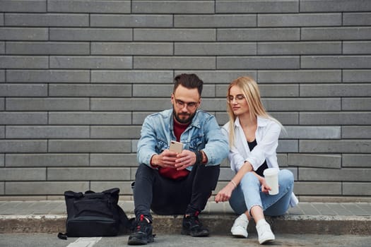 Young stylish man with woman in casual clothes sitting outdoors together. Conception of friendship or relationships.