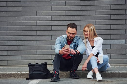 Young stylish man with woman in casual clothes sitting outdoors together. Conception of friendship or relationships.