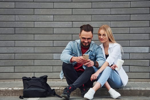 Young stylish man with woman in casual clothes sitting outdoors together. Conception of friendship or relationships.