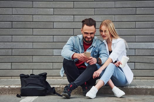 Young stylish man with woman in casual clothes sitting outdoors together. Conception of friendship or relationships.