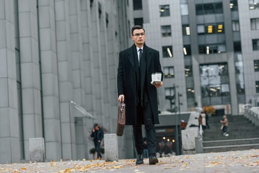 Walking forward. Businessman in black suit and tie is outdoors in the city.