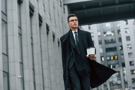 Walking forward. Businessman in black suit and tie is outdoors in the city.