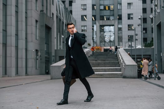 Phone in hand. Businessman in black suit and tie is outdoors in the city.