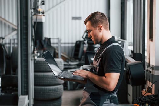 Holding laptop in hands. Man in uniform is working in the auto service.