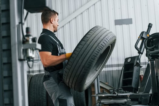 Walking and holding tyre. Man in uniform is working in the auto service.