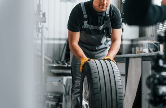 Close up view of wheel. Man in uniform is working in the auto service.