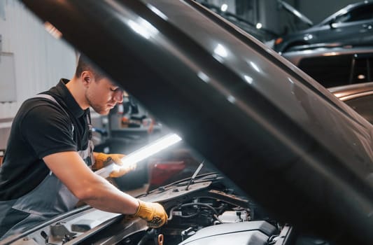 Under the hood. Man in uniform is working in the auto service.