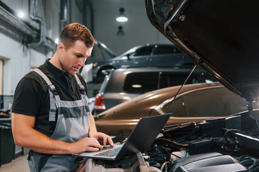 Side view. Man in uniform is working in the auto service.
