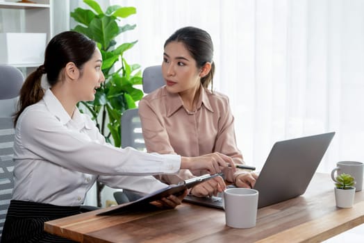 Two young office lady colleagues collaborating in modern office workspace, engaging in discussion and working together on laptop, showcasing their professionalism as modern office worker. Enthusiastic