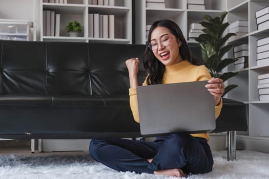 Happy young Asian business woman successful excited raised hand rejoicing with laptop at home...