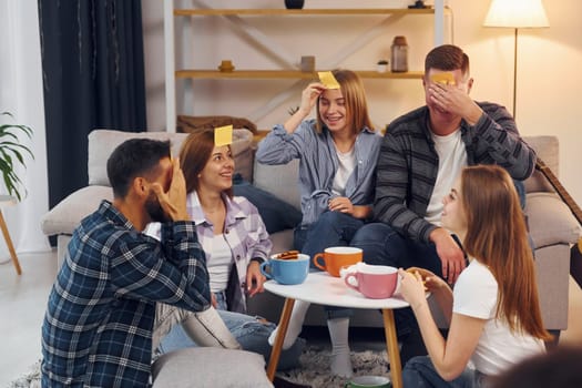Playing who am I game. Group of friends have party indoors together.