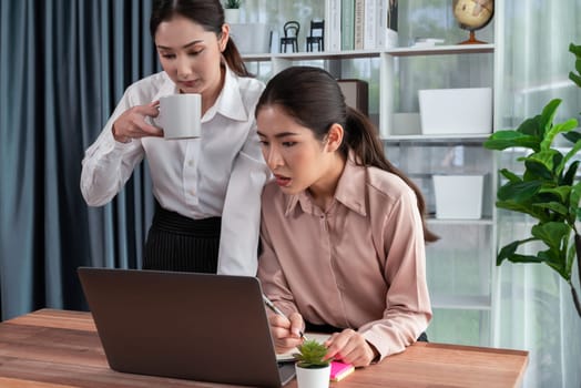 Two young office lady colleagues collaborating in modern office workspace, engaging in discussion and working together on laptop, showcasing their professionalism as modern office worker. Enthusiastic