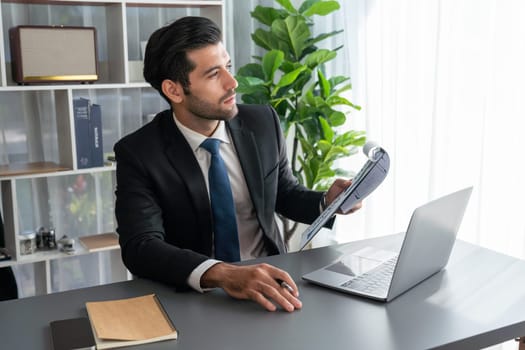 Modern professional businessman at modern office desk using laptop to work and write notes. Diligent office worker working on computer notebook in his office work space. fervent