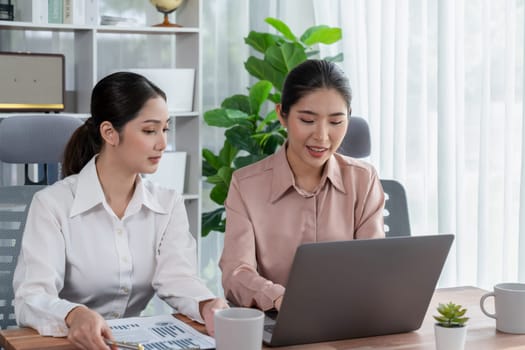 Two young office lady colleagues collaborating in modern office workspace, engaging in discussion and working together on laptop, showcasing their professionalism as modern office worker. Enthusiastic