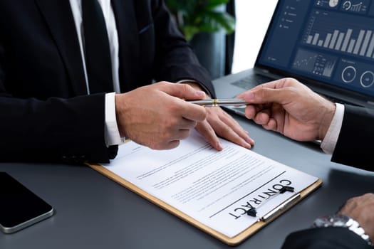 Two businesspeople sit across the desk as business deal is taking place. Corporate attorney giving a pen for client or partner to sign contract paper, sealing the deal with signature. Fervent