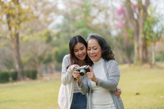 Asian teenage mother and daughter walking in park with camera to capture memories.