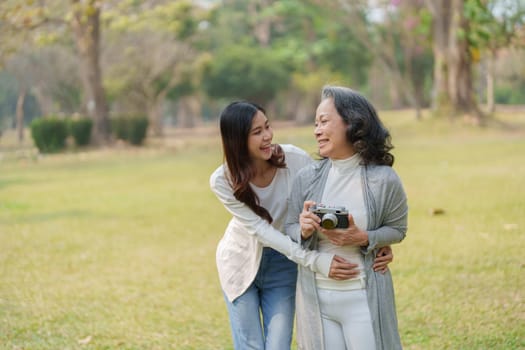 Asian teenage mother and daughter walking in park with camera to capture memories.