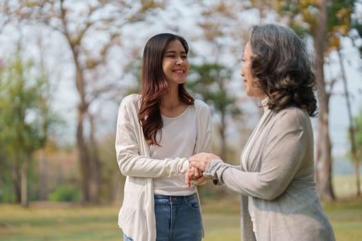 Adult daughter holding her elderly mother hand with love and walk together in park.