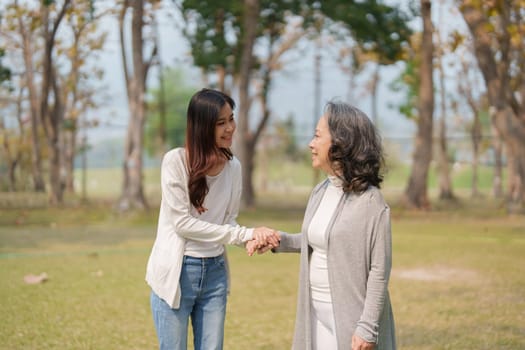 Adult daughter holding her elderly mother hand with love and walk together in park.