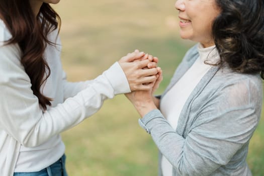 Adult daughter holding her elderly mother hand with love and walk together in park.