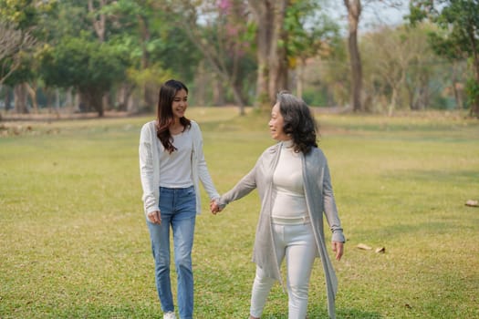 Adult daughter holding her elderly mother hand with love and walk together in park.