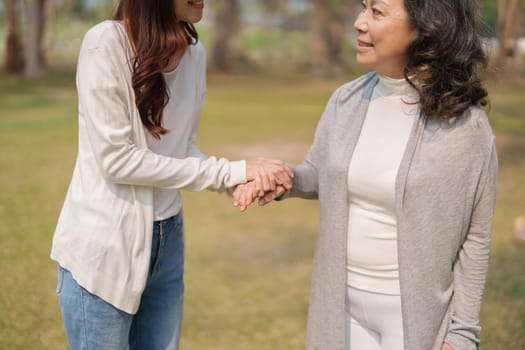 Adult daughter holding her elderly mother hand with love and walk together in park.