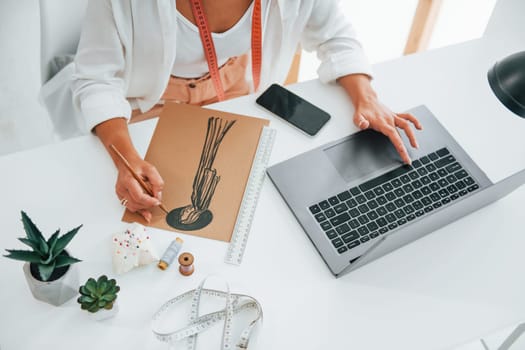 Using laptop. Seamstress is in her office that is with different clothes.
