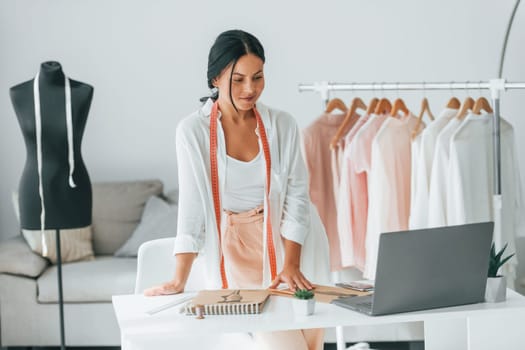 With laptop. Seamstress is in her office that is with different clothes.