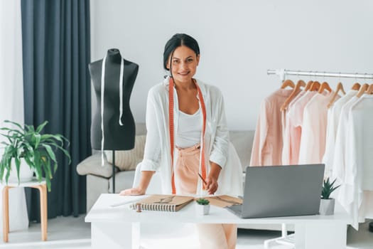 Seamstress is standing in her office that is with different clothes.