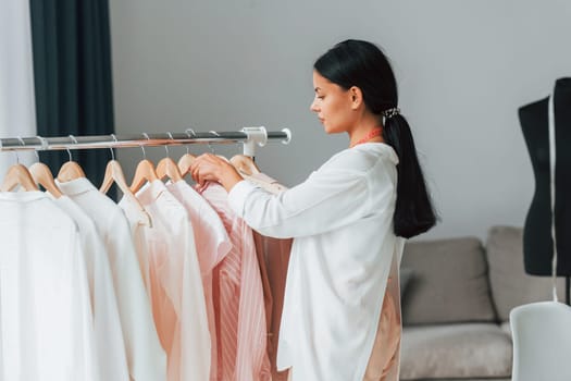 Seamstress is standing in her office that is with different clothes.